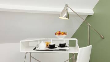 A white desk with a bowl of fruit, two black cups, a teapot, and a glass of orange juice.
