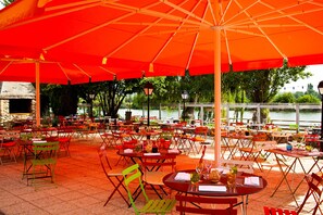 An outdoor dining area with red umbrellas, tables, and chairs arranged around a lake. - Les Canisses (Saint-Pierre-la-Garenne)
