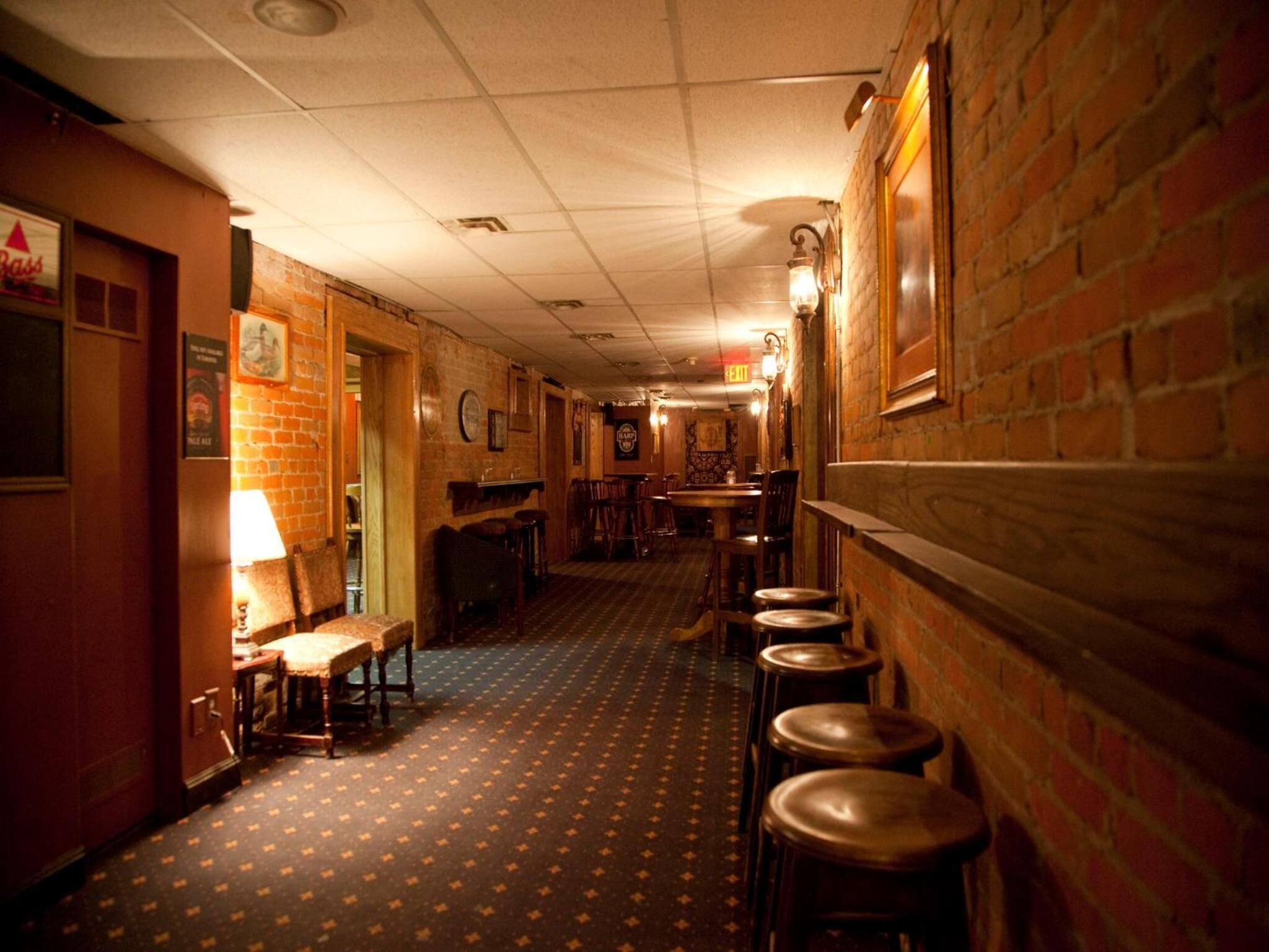 A narrow hallway with brick walls, wooden chairs, and tables.