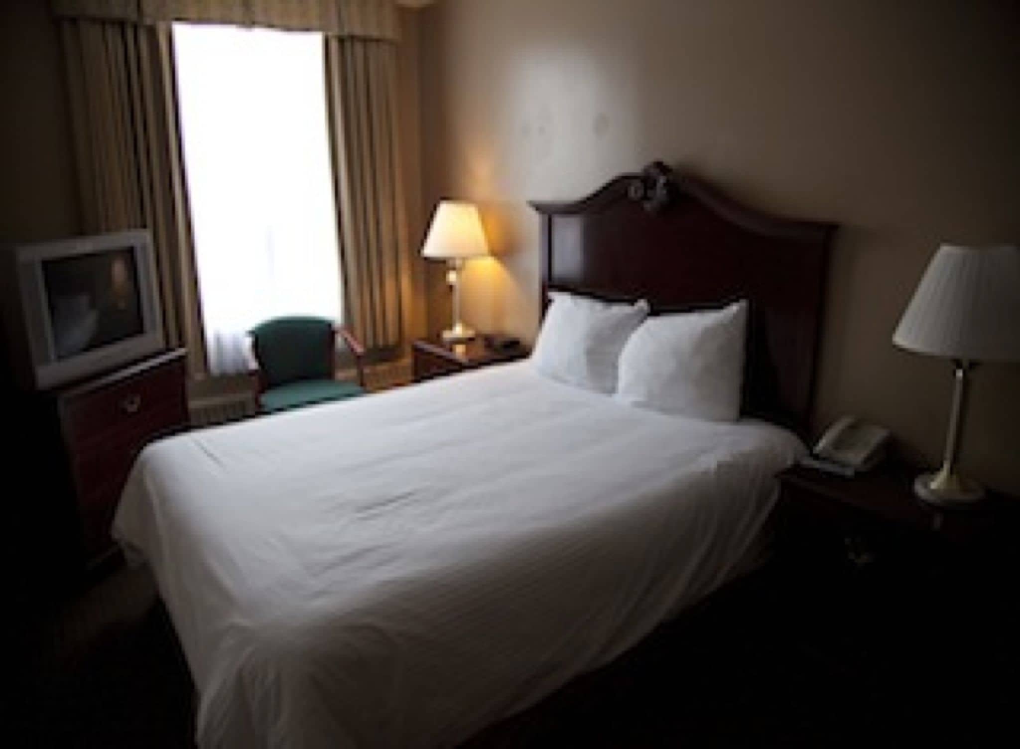 A hotel room with a large bed, a television on a dresser, a lamp, and a chair.