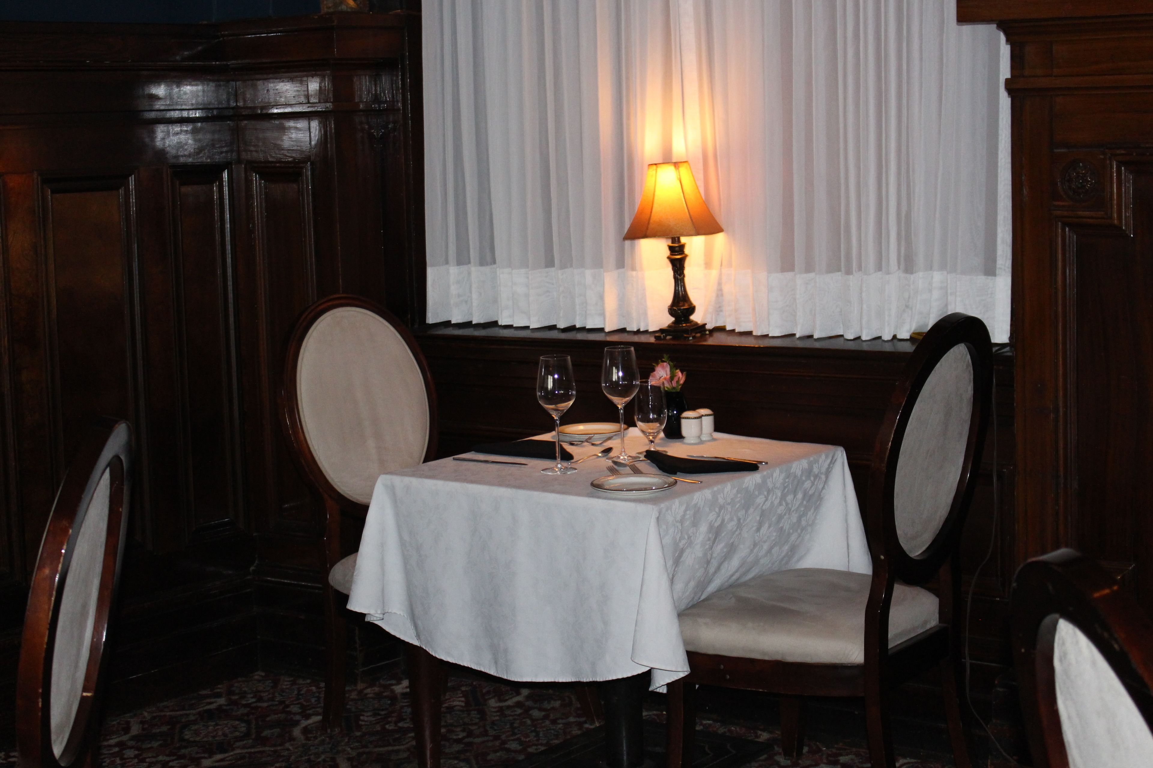 A dining table set with two wine glasses, a plate, and a small vase.