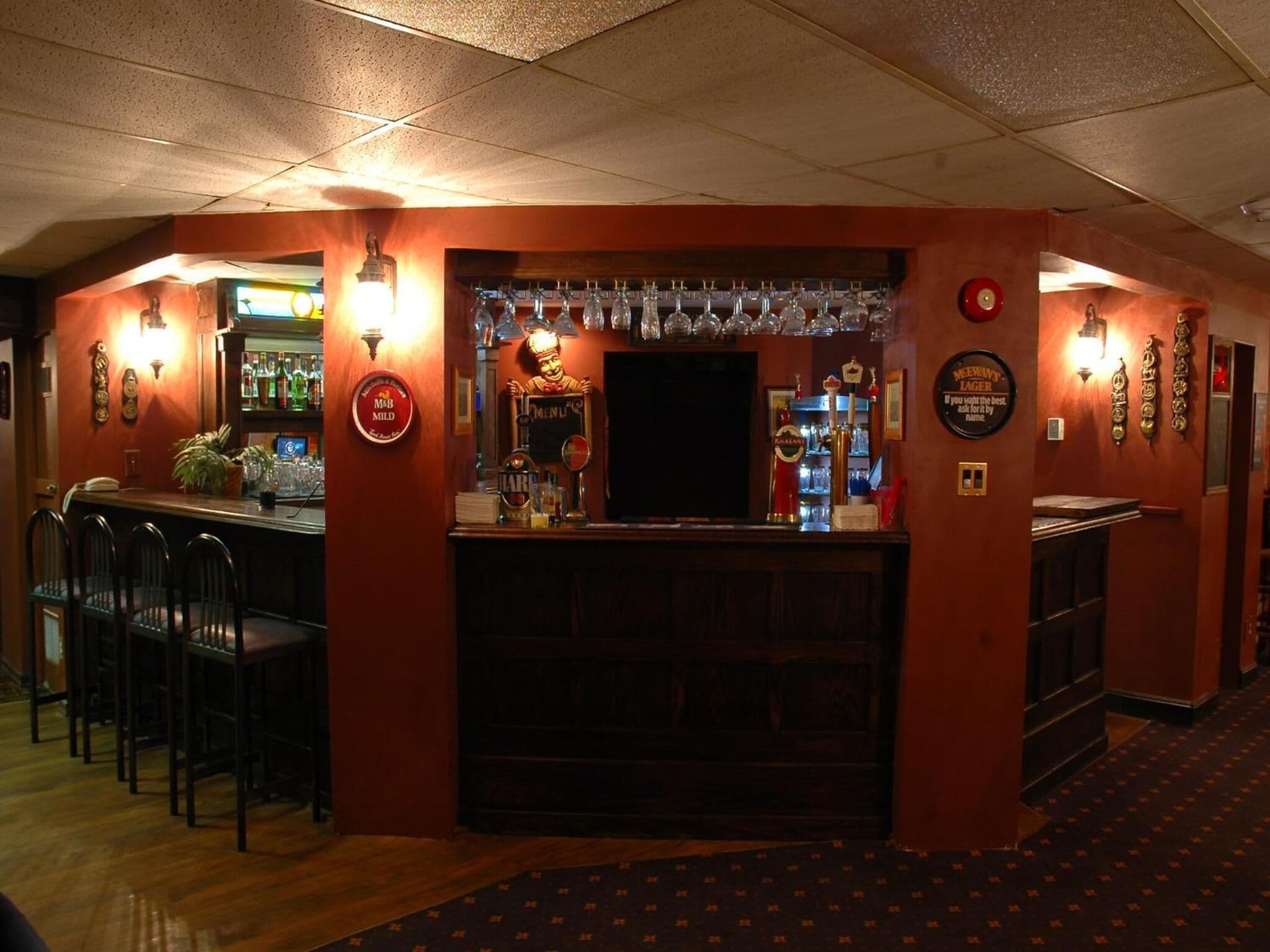 A bar area with a counter, stools, and a variety of bottles and glasses.