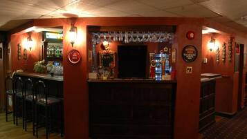 A bar area with a counter, stools, and a variety of bottles and glasses.
