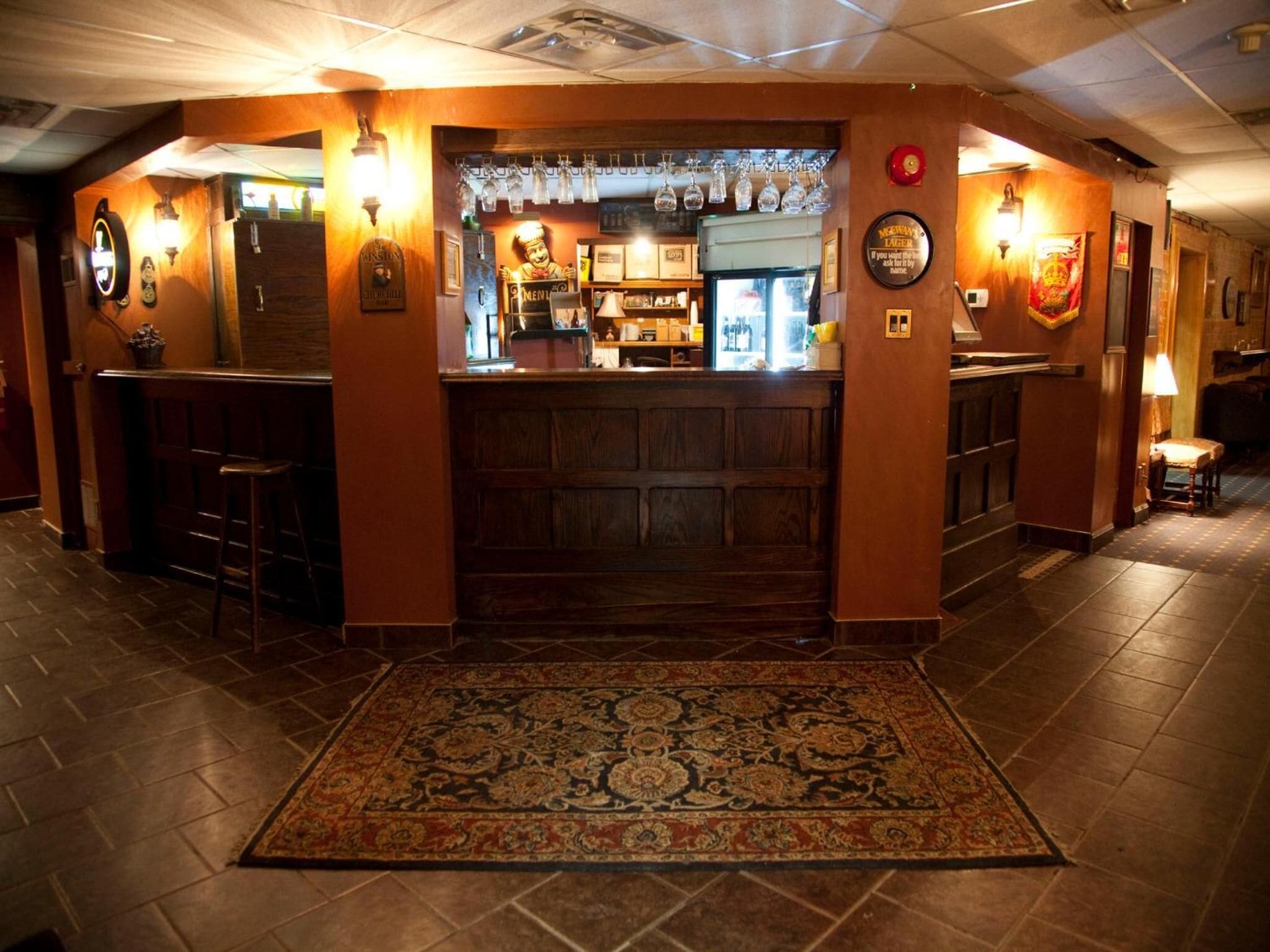 Zona de bar amb un taulell de fusta, gots penjants i una catifa amb un disseny decoratiu al sòl.