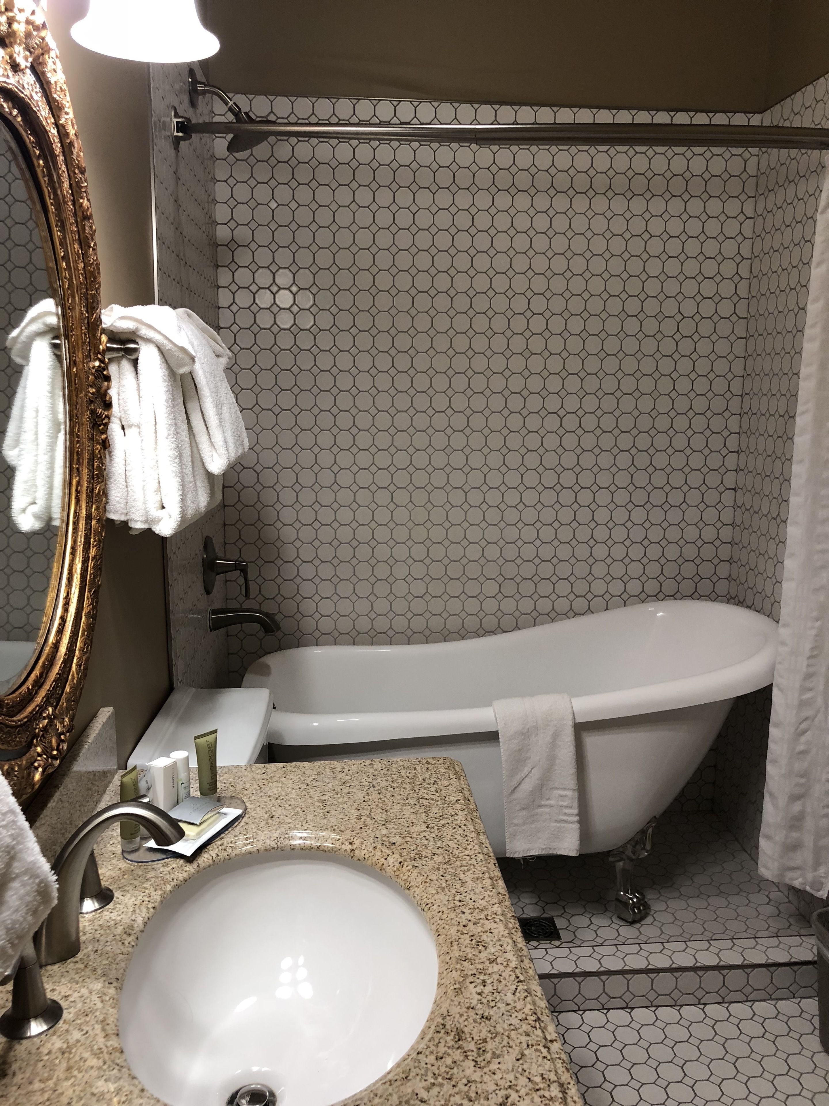 Une salle de bain dotée d’une baignoire sur pieds, d’un lavabo avec un plan de travail en granit et d’un miroir avec un cadre doré.