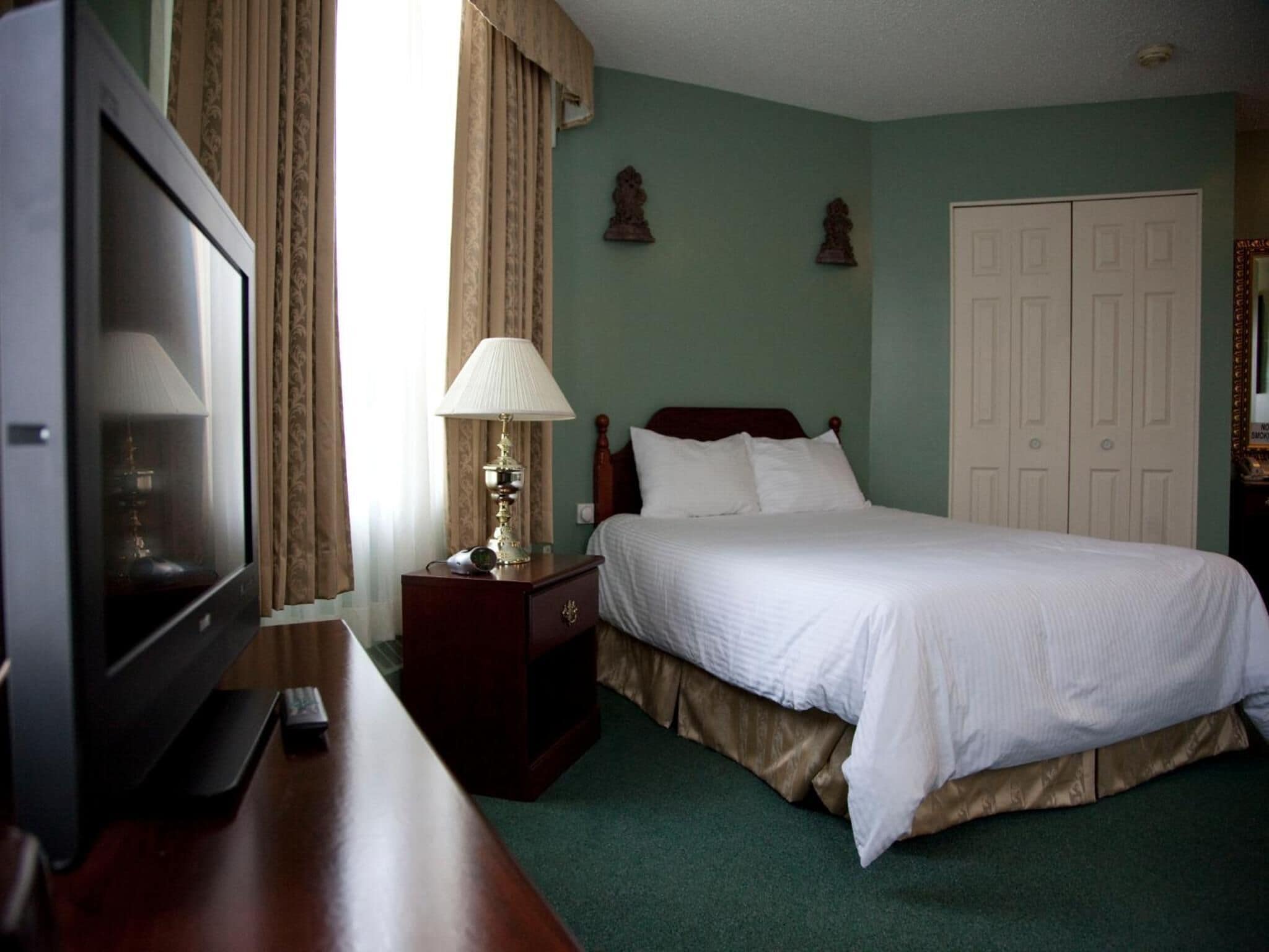 Ein Hotelzimmer mit Bett, Fernseher, Lampe und Kleiderschrank.