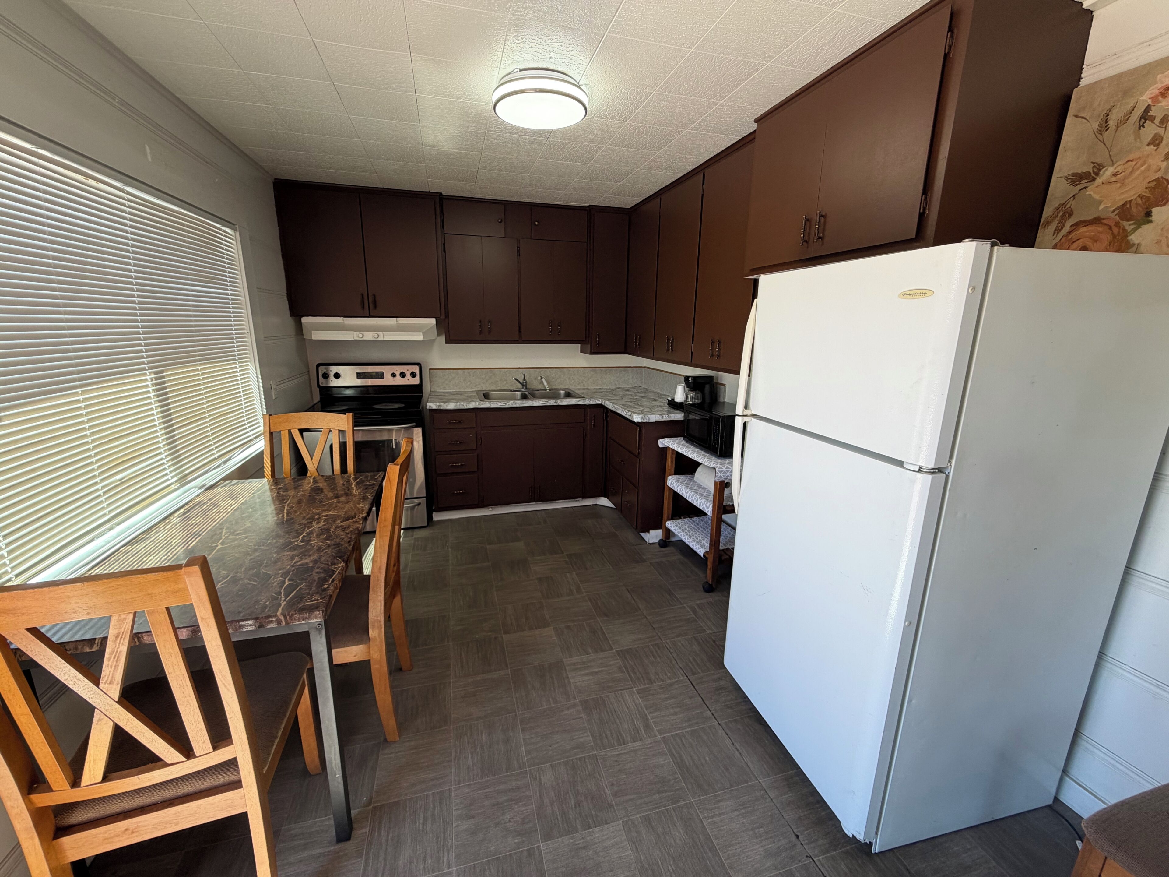 A compact kitchen with dark wooden cabinets, a white refrigerator, a stove, and a dining table with chairs.