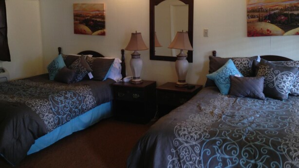 A room with two beds, each with patterned bedding and multiple pillows. There are bedside lamps and a large mirror on the wall. - Sonoma Lodge (Bend)