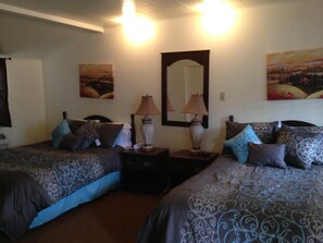 A room with two beds, each with patterned bedding and multiple pillows. There are bedside lamps and a large mirror on the wall. - Sonoma Lodge (Bend)