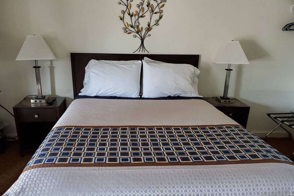 A neatly made bed with a patterned bedspread, two bedside tables with lamps, and a wall-mounted decorative piece above the bed.