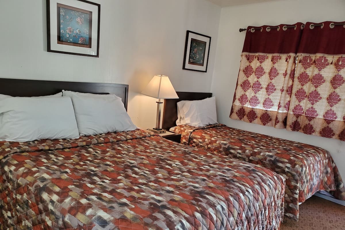 A double bed with a patterned bedspread, a bedside table with a lamp, and two framed pictures on the wall.