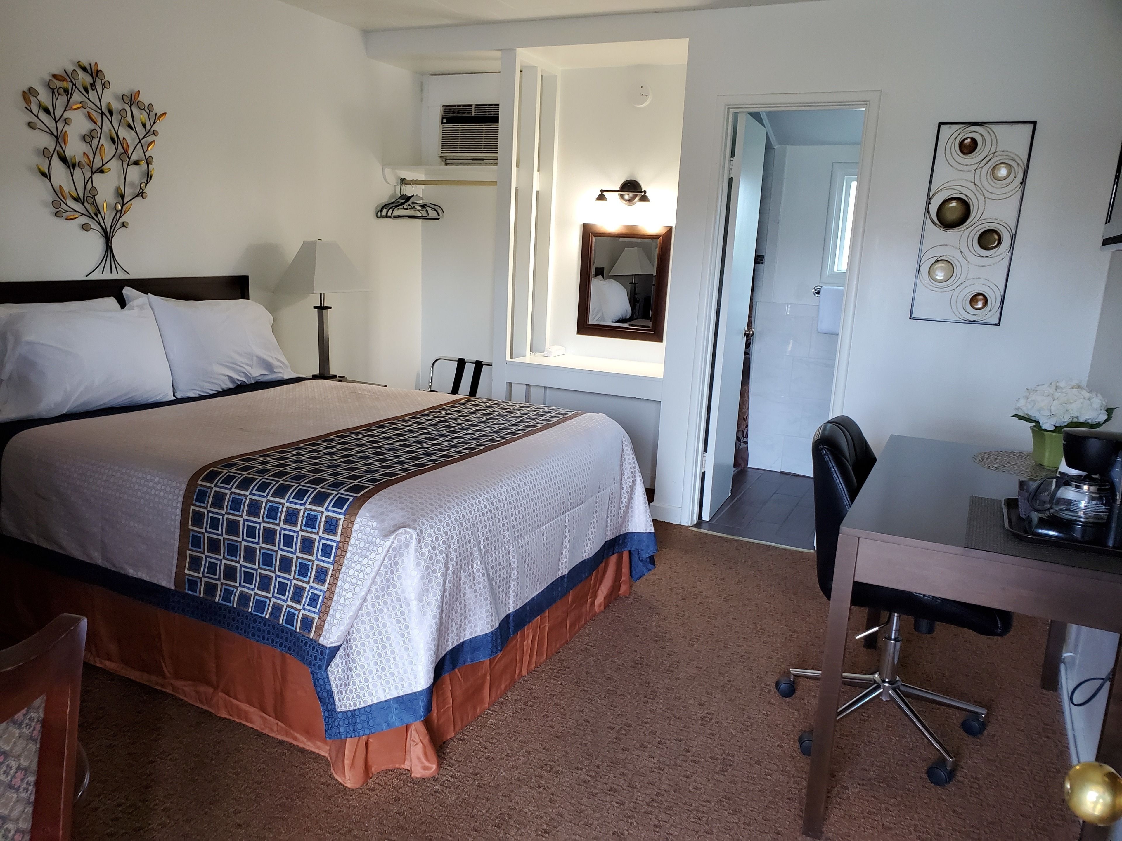 Una habitación de hotel con cama, escritorio, silla, lámpara, espejo y decoración en la pared.
