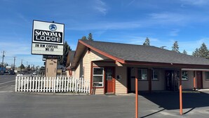 A building with a sign for 'SONOMA LODGE' and a parking lot. - Sonoma Lodge (Bend)