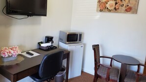 A compact hotel room with a flat-screen TV, a microwave, a small refrigerator, a desk with a chair, a coffee maker, and a decorative flower arrangement. - Sonoma Lodge (Bend)