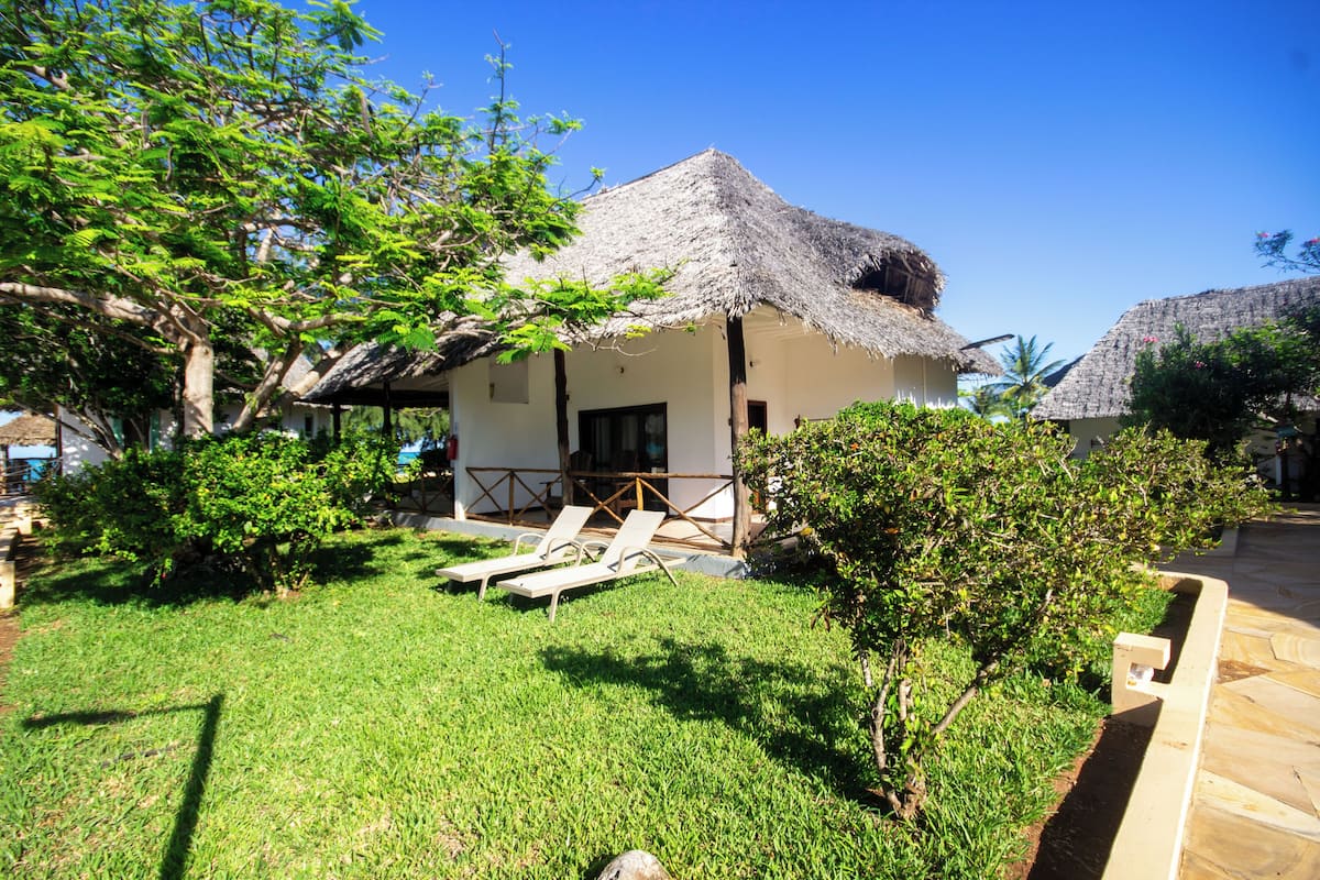 A thatched-roof house with a lawn and two lounge chairs.