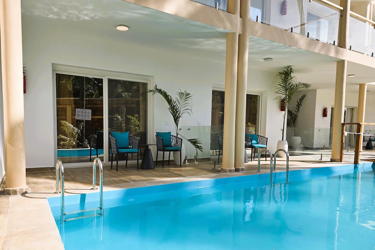A pool area with chairs and a table, surrounded by large pillars and glass doors leading to an outdoor space.