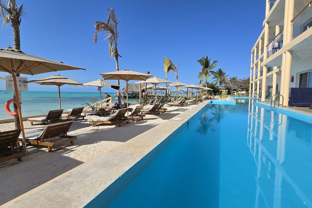 A poolside area with lounge chairs and umbrellas, a clear blue pool, and a view of the ocean.