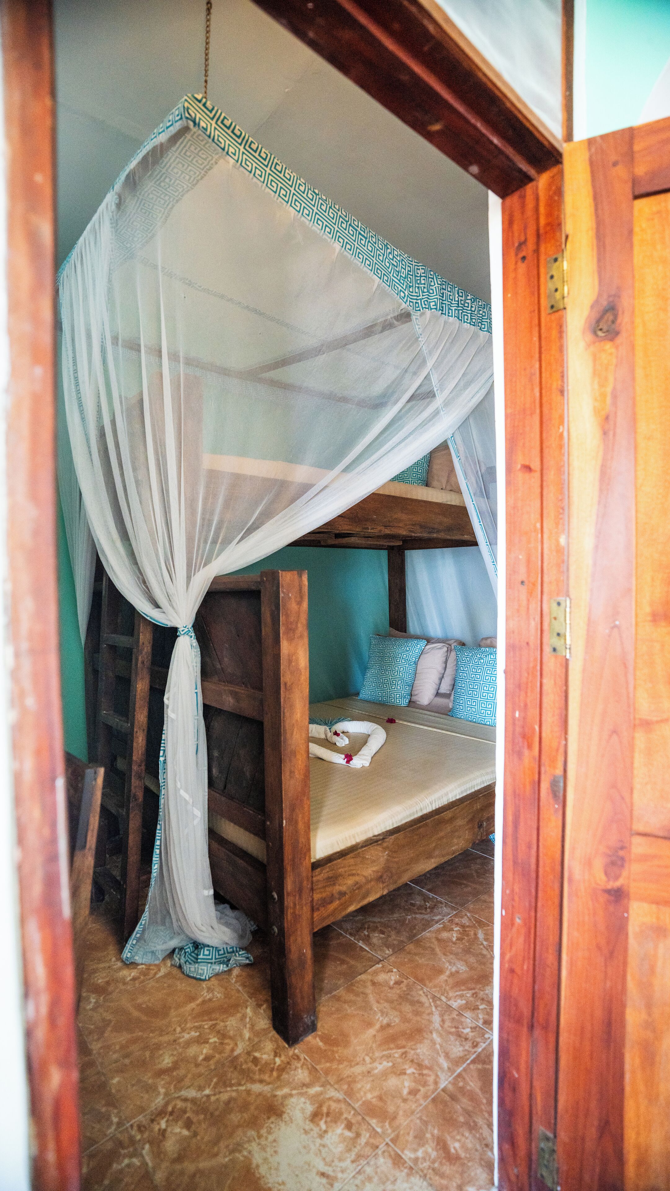 Una cama de madera rústica con mosquitero, una mesita de noche pequeña y almohadas estampadas.