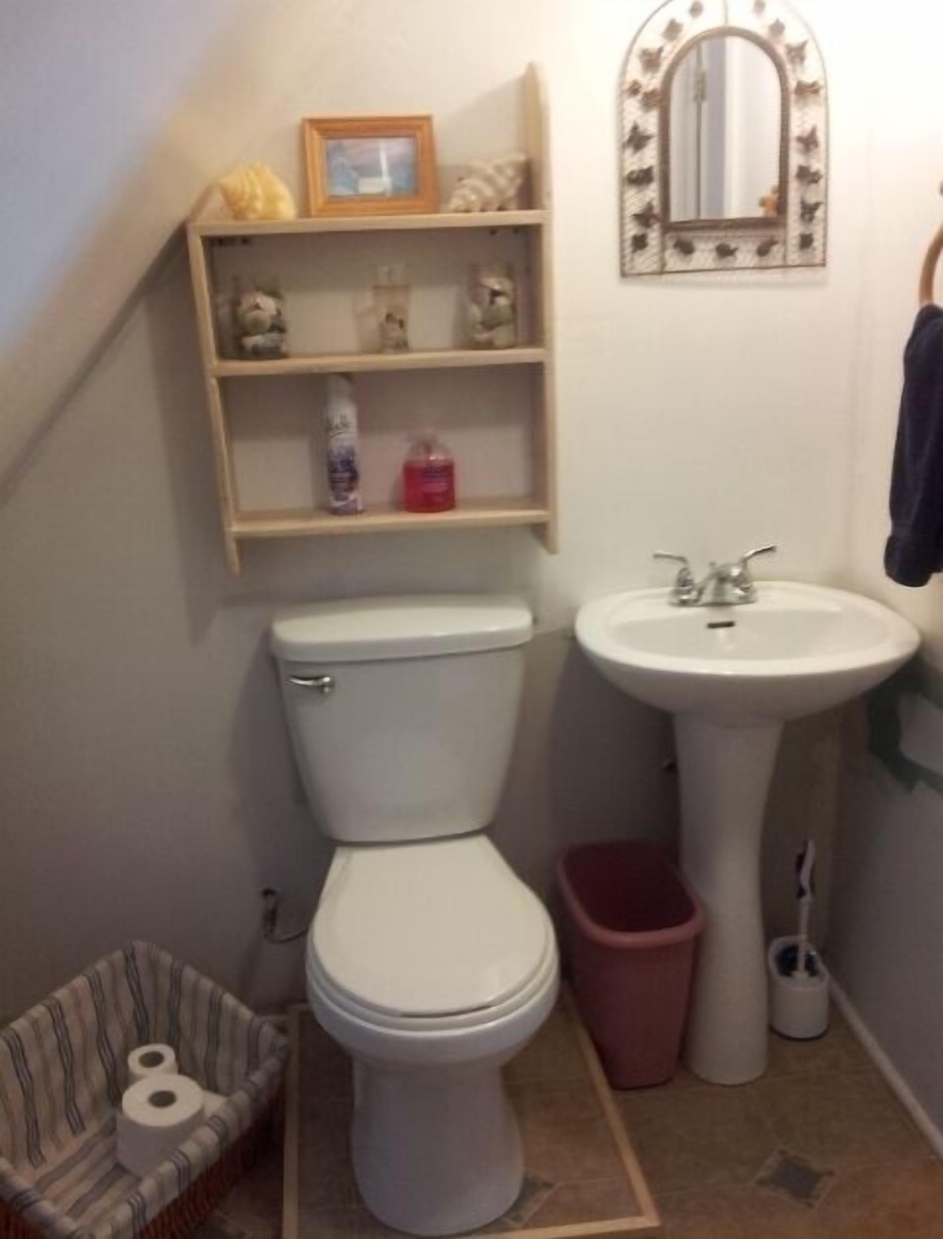 Een compacte badkamer met toilet, wastafel en planken boven het toilet.