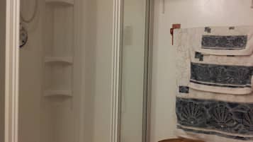 Et bruseområde med glasdør, en fletkurv og en hylde med foldede håndklæder.