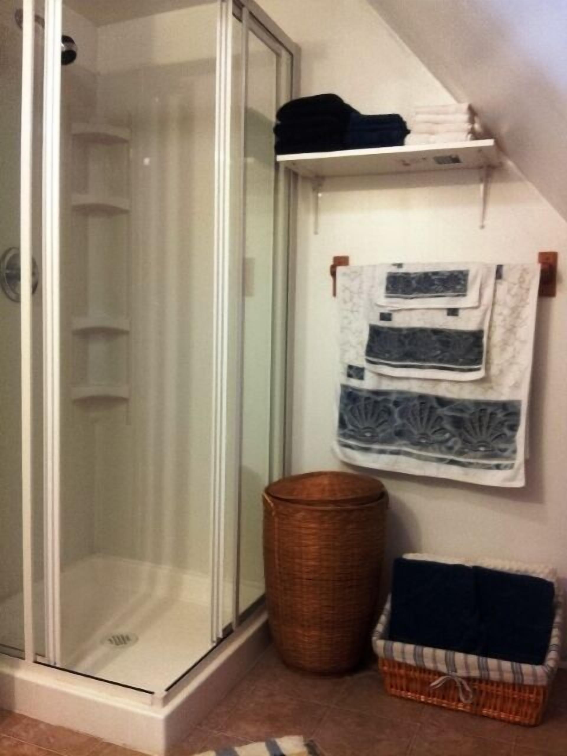 Ein Badezimmer mit einer Glasdusche, einem Korbwäschesammler und einem Wäschekorb.