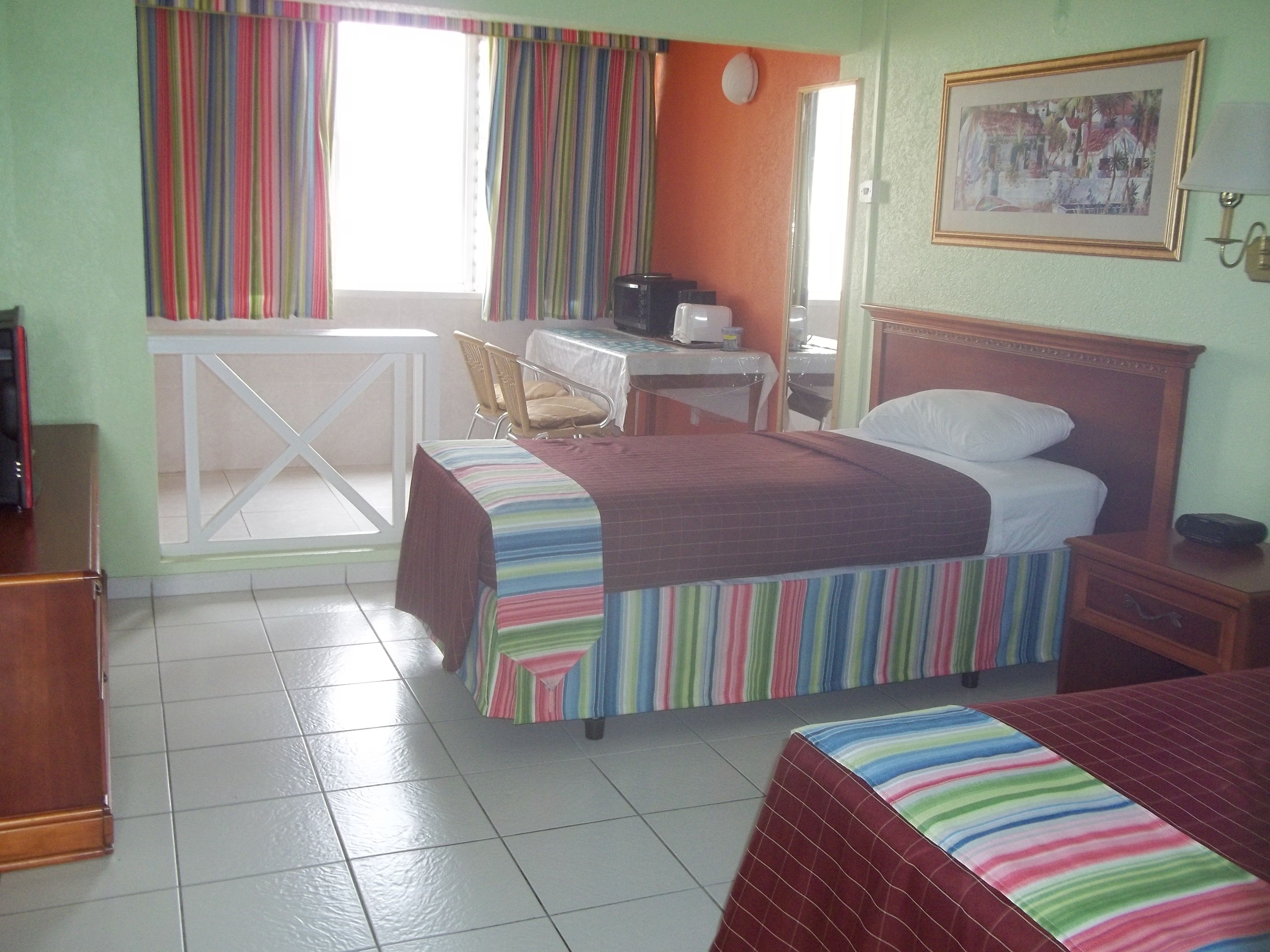 A hotel room with two beds, a desk, a chair, a small table, and a window with curtains.