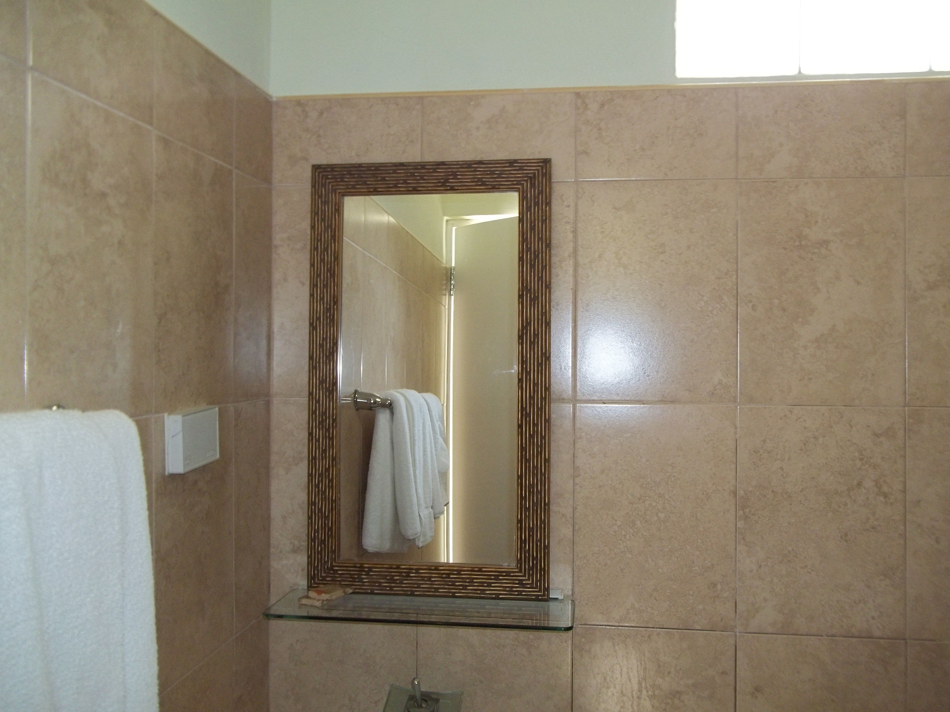 A bathroom with a large mirror, a towel rack, and a glass shelf.