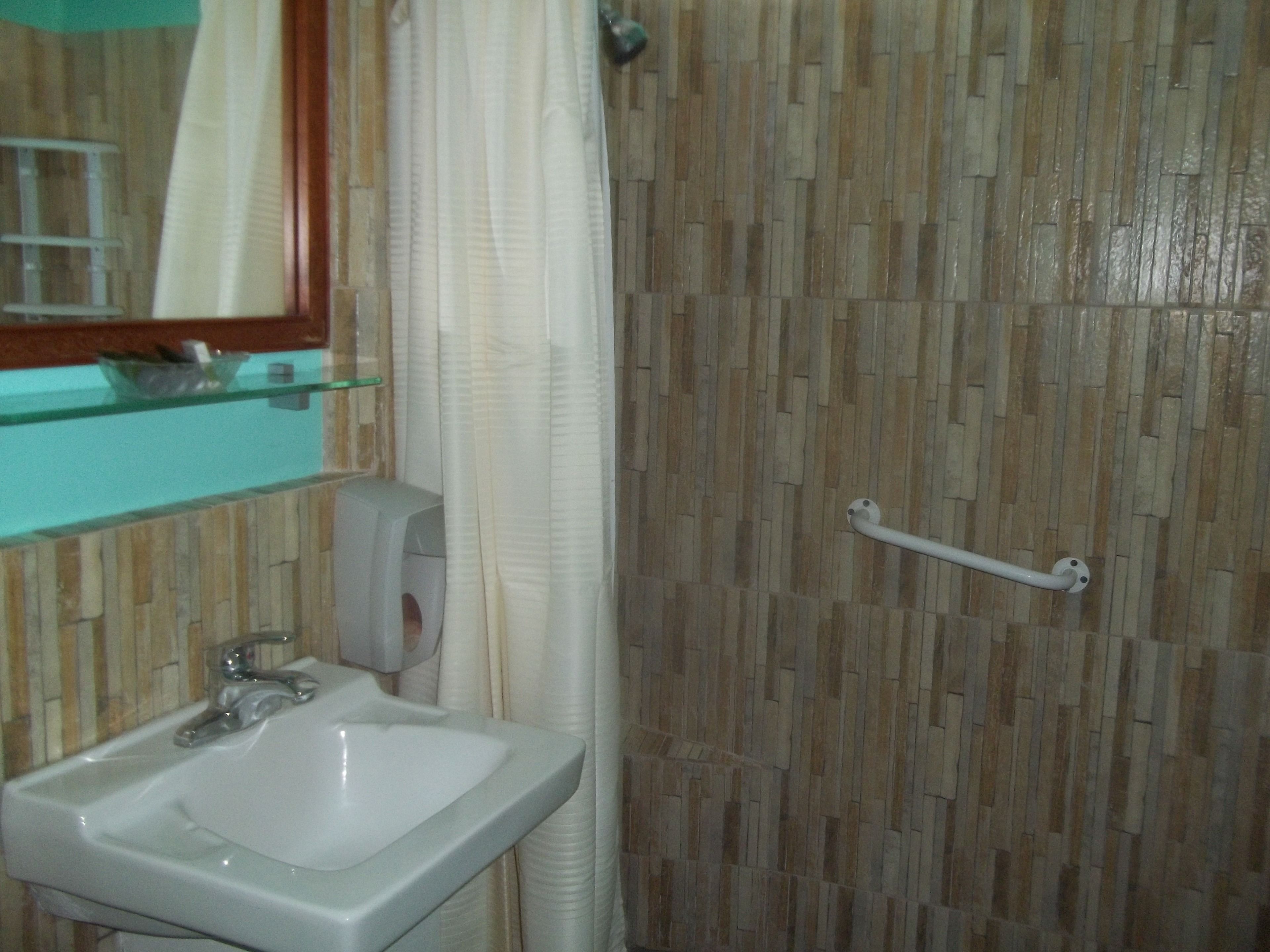 A bathroom with a white sink, a mirror, and a shower area with a textured wall.