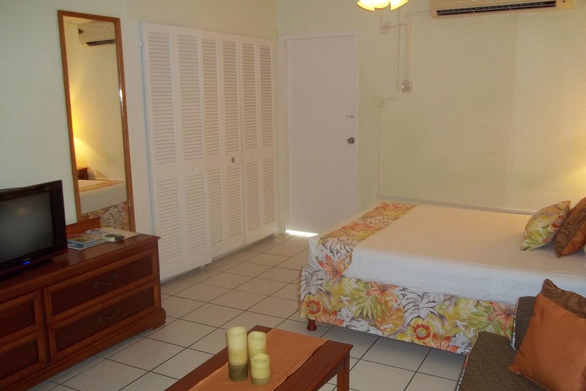 Une chambre à coucher avec un lit, un téléviseur posé sur une commode, un miroir, une armoire et une petite table avec des bougies.