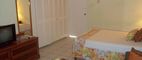 Une chambre à coucher avec un lit, un téléviseur posé sur une commode, un miroir, une armoire et une petite table avec des bougies.