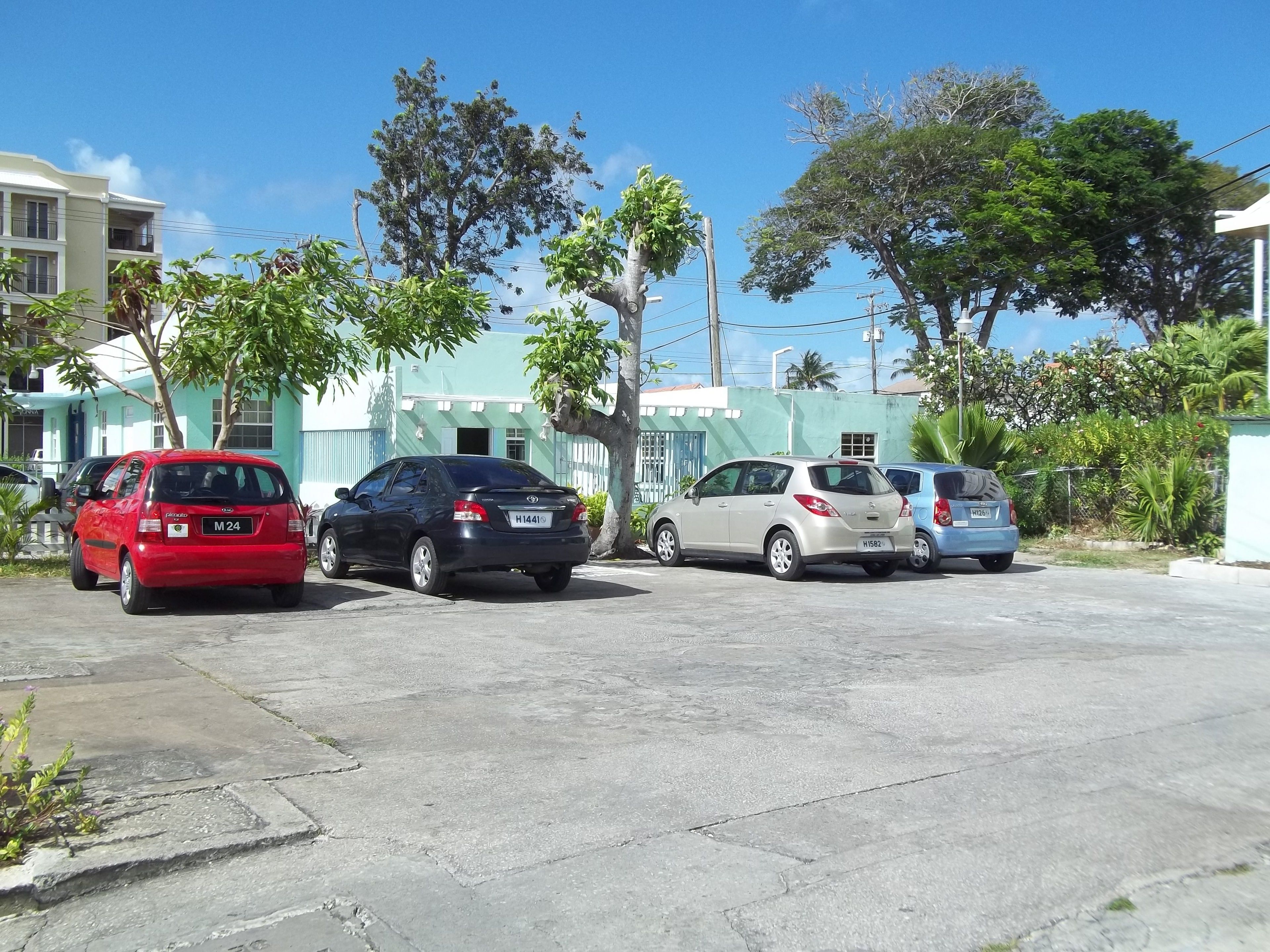 Un área de estacionamiento con tres coches aparcados frente a un edificio de fachada verde.