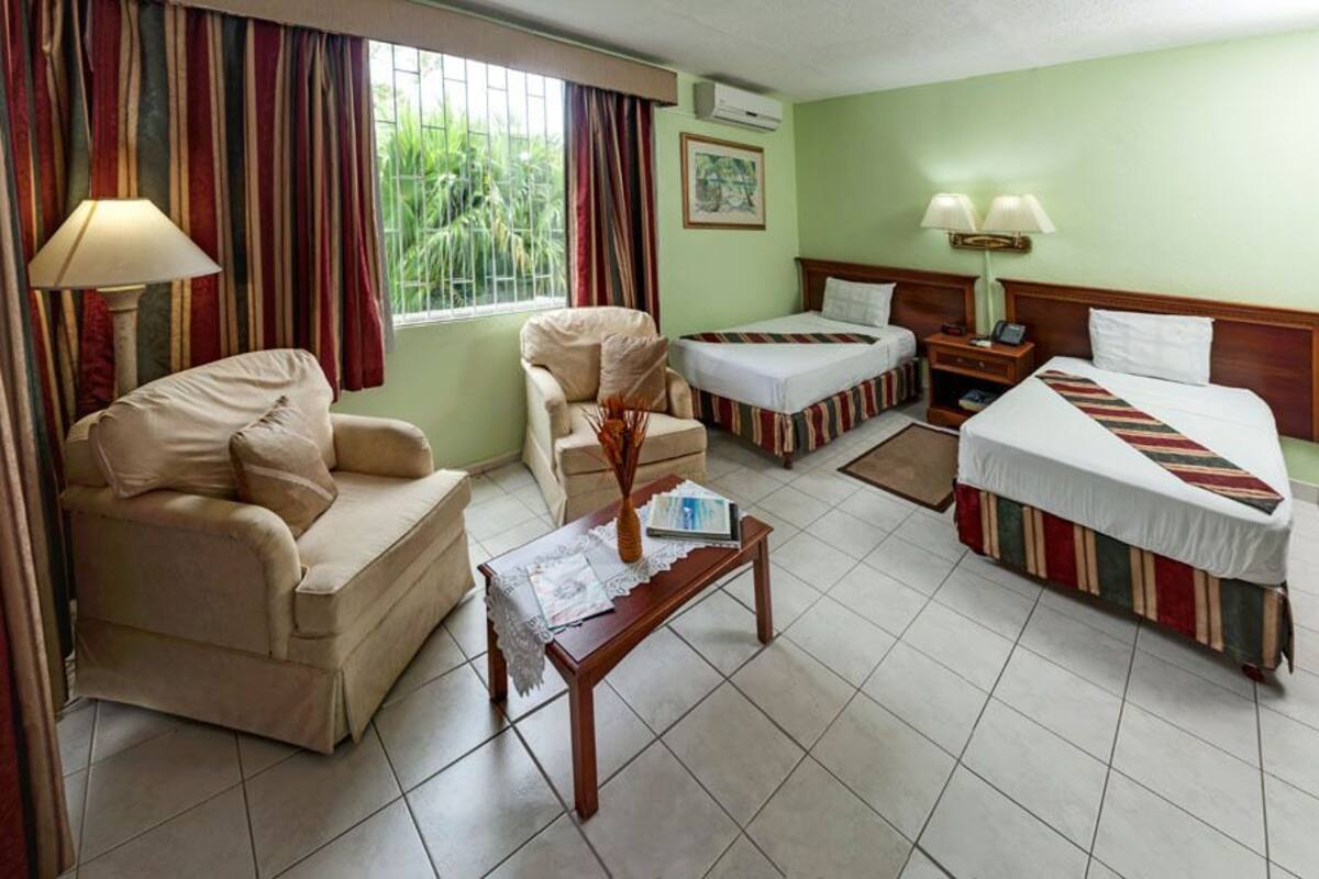 Une chambre d’hôtel avec un canapé, deux lits simples, une petite table et une fenêtre avec des rideaux.