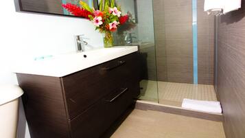 Un baño con tocador de madera oscura, un lavabo blanco y cabina de ducha con mampara de vidrio.