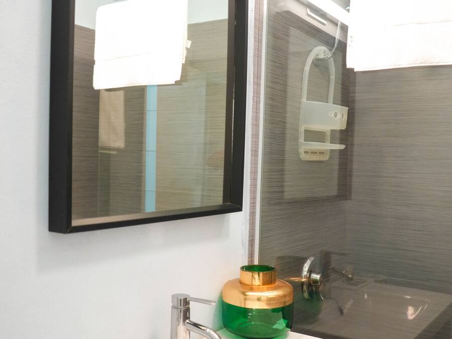 Un baño con un lavabo blanco, un espejo y un dispensador de jabón verde.
