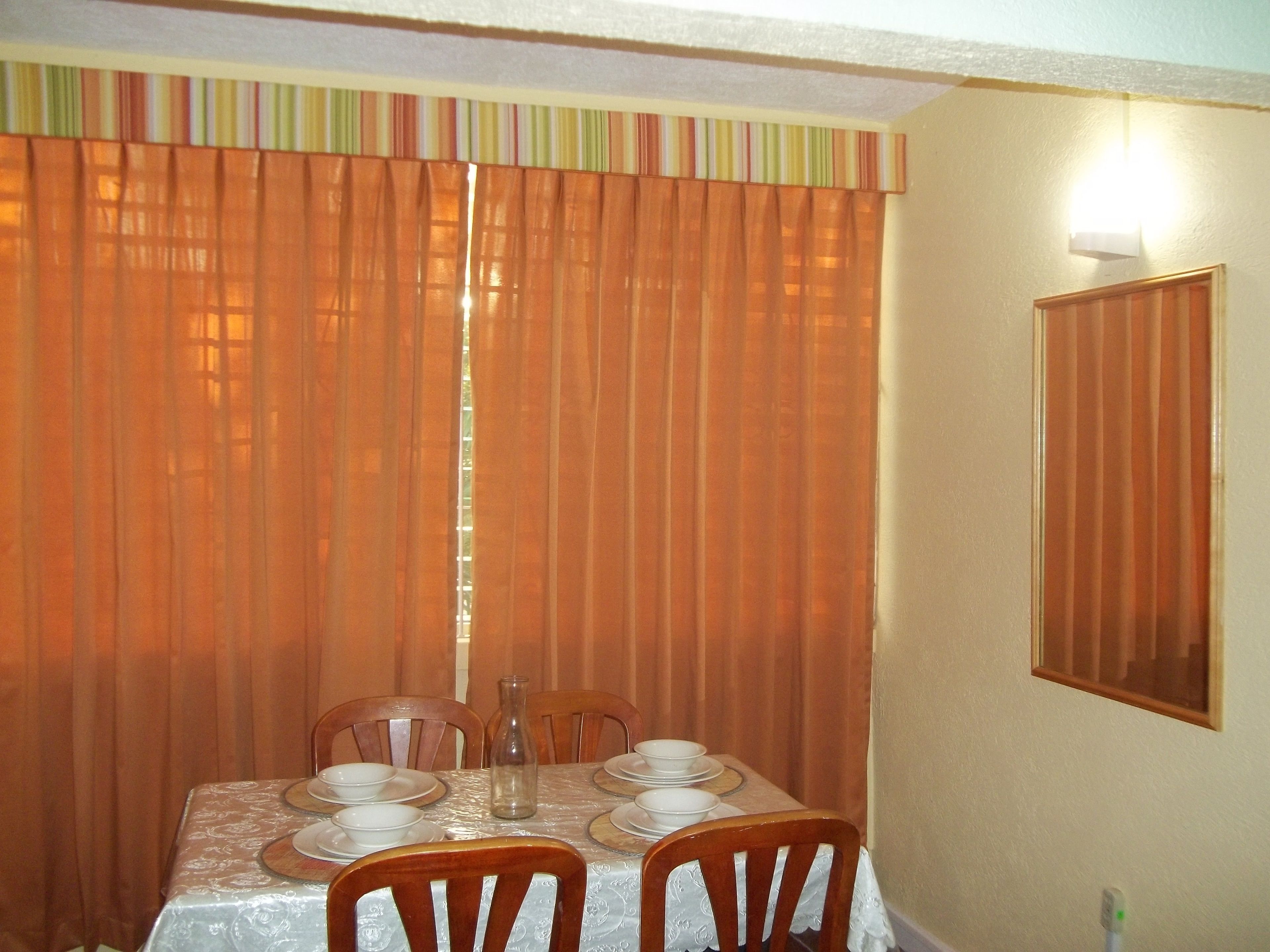 A dining area with a table set for four, chairs, a vase, and a wall-mounted light.