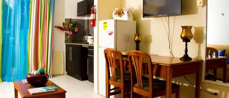 A hotel room with a bed, a desk, chairs, a television, a refrigerator, and a kitchen area.