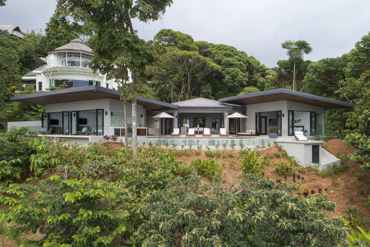 A modern house with a large patio area, surrounded by lush greenery and trees.