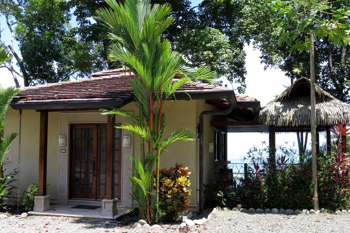 A small building with a tiled roof, a wooden door, and a thatched structure nearby.
