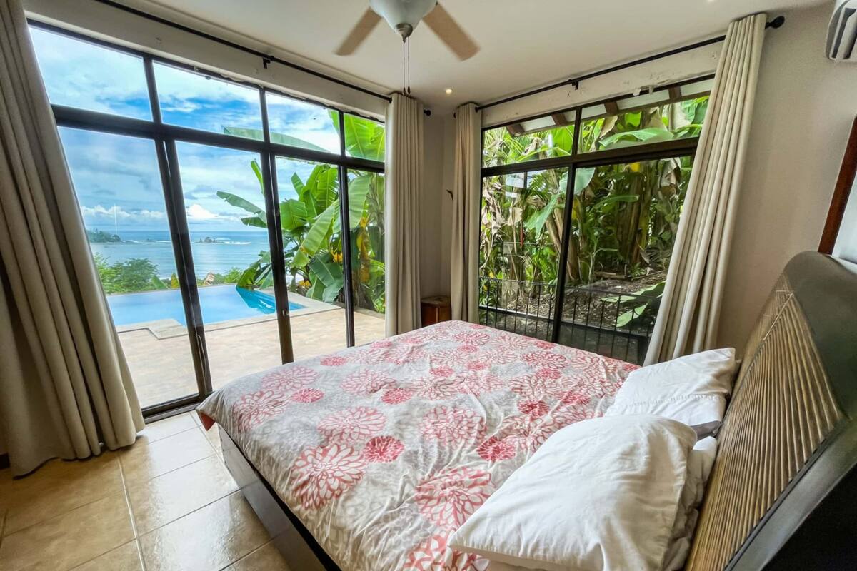 A bedroom with a large bed, a view of the ocean, and a ceiling fan.
