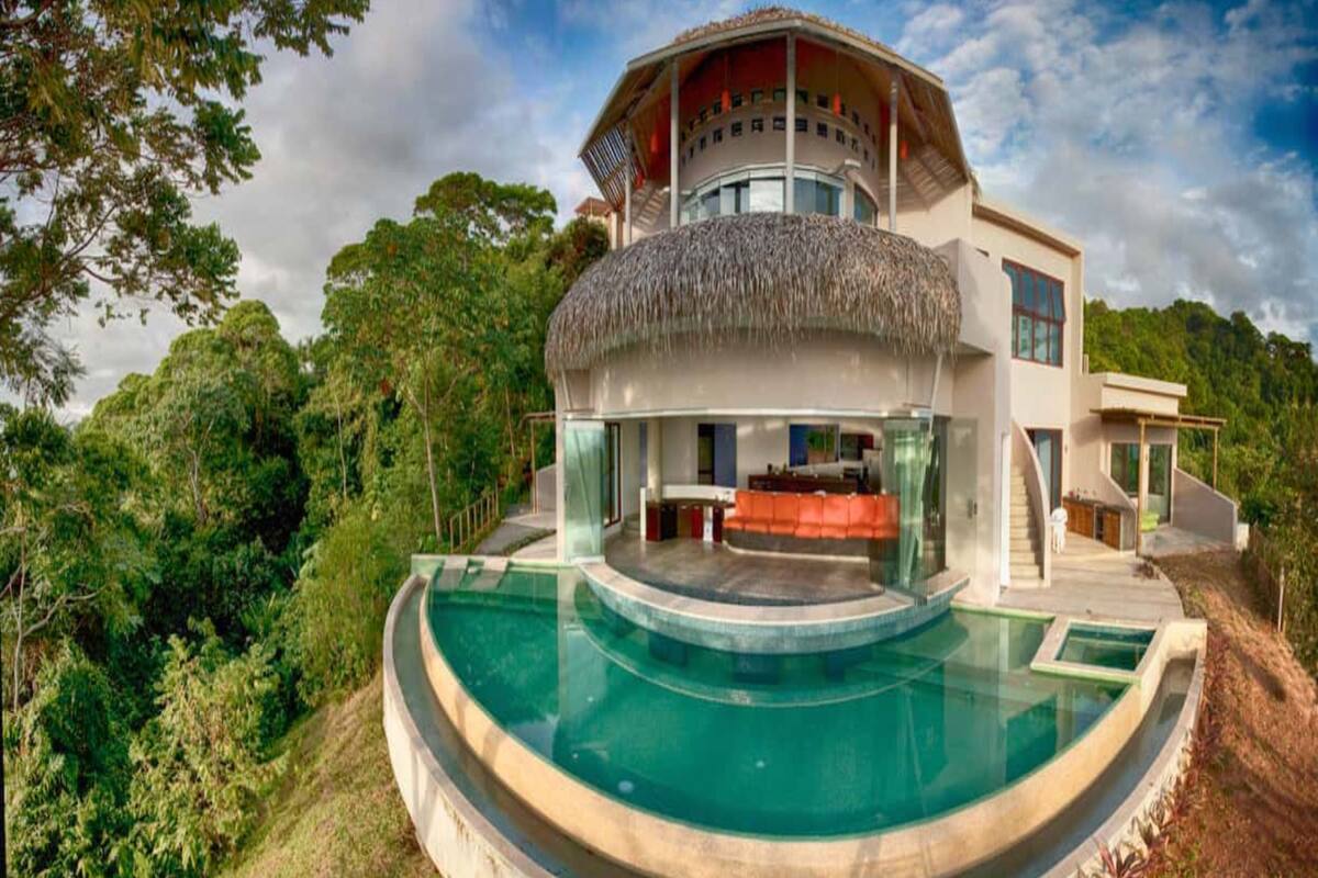 A modern house with a circular pool, a thatched roof, and a large outdoor seating area.