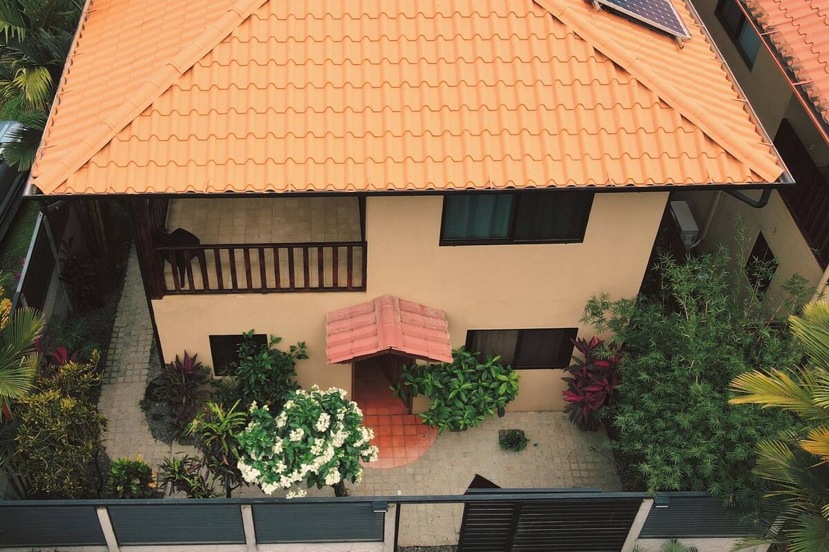 A two-story house with a tiled roof, a balcony, and solar panels.