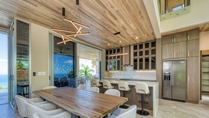 Una cocina moderna con una mesa de comedor de madera y sillas blancas, una isla integrada con taburetes altos y un refrigerador grande.