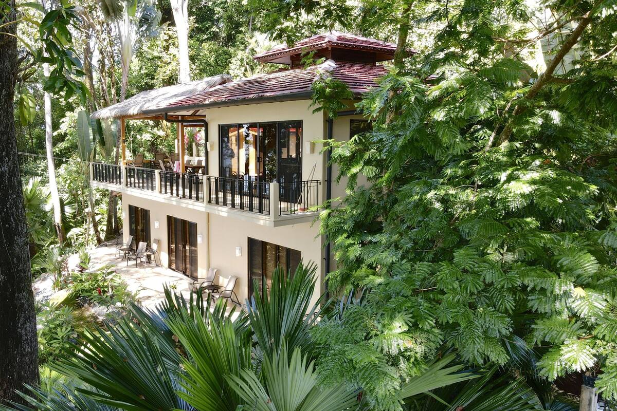 A two-story building with a balcony, surrounded by lush greenery.