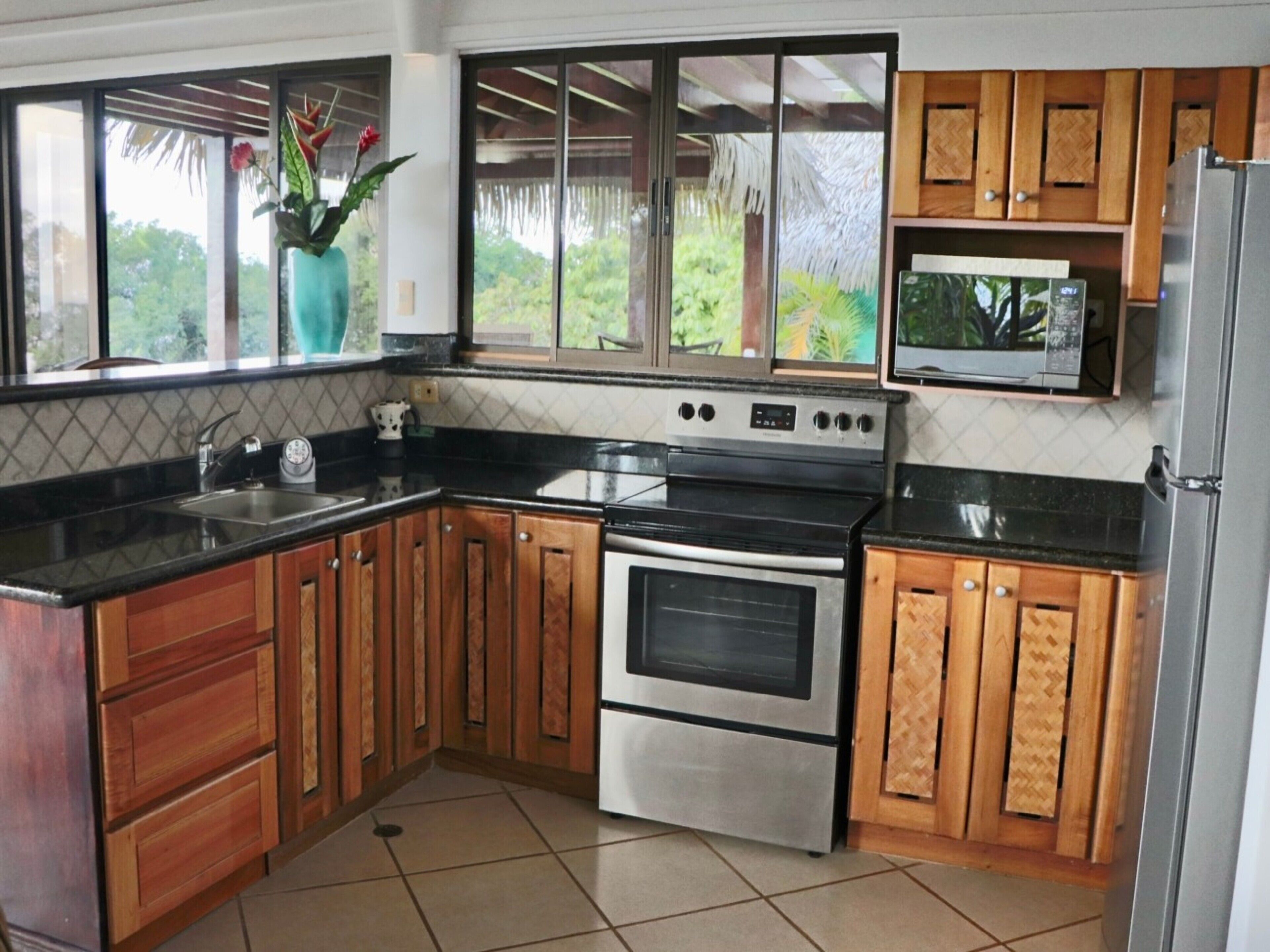 A kitchen with wooden cabinets, a stainless steel oven, a microwave, and a window with a view of greenery.