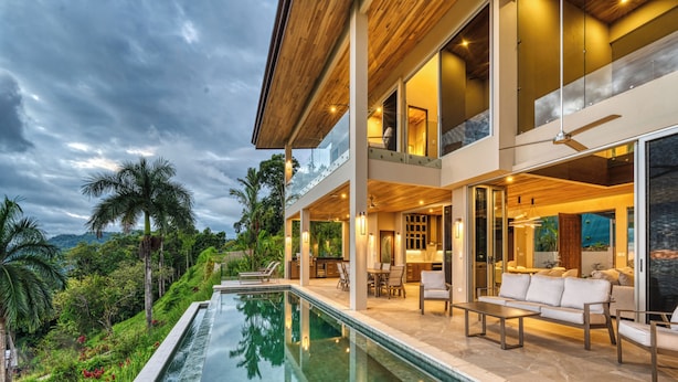 Una casa moderna con una piscina grande, mobiliario de exterior y vistas al follaje circundante.