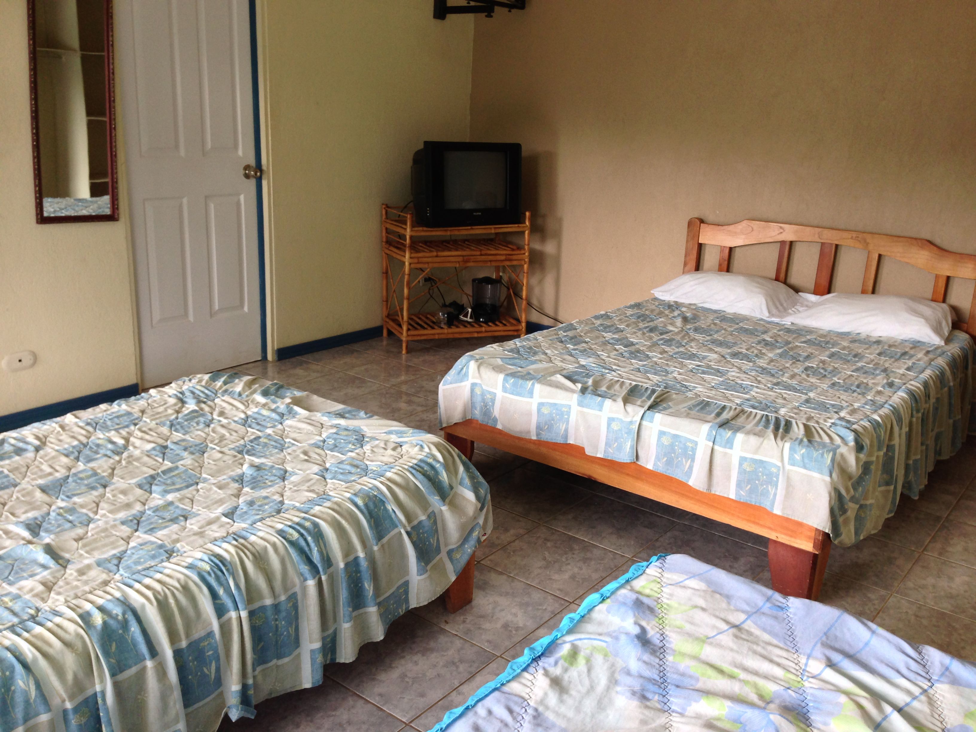 Una habitación con dos camas, un televisor sobre un soporte de madera y una puerta.