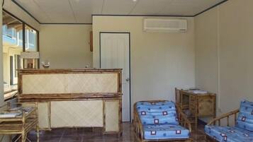 A room with a wooden reception desk, two wicker chairs, a sofa, and a tiled floor.