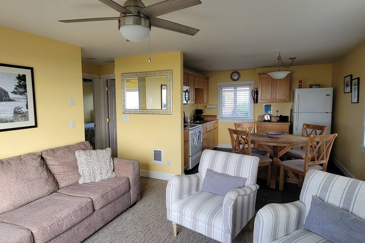 A compact living space with a sofa, armchairs, a dining table, and a kitchen area.