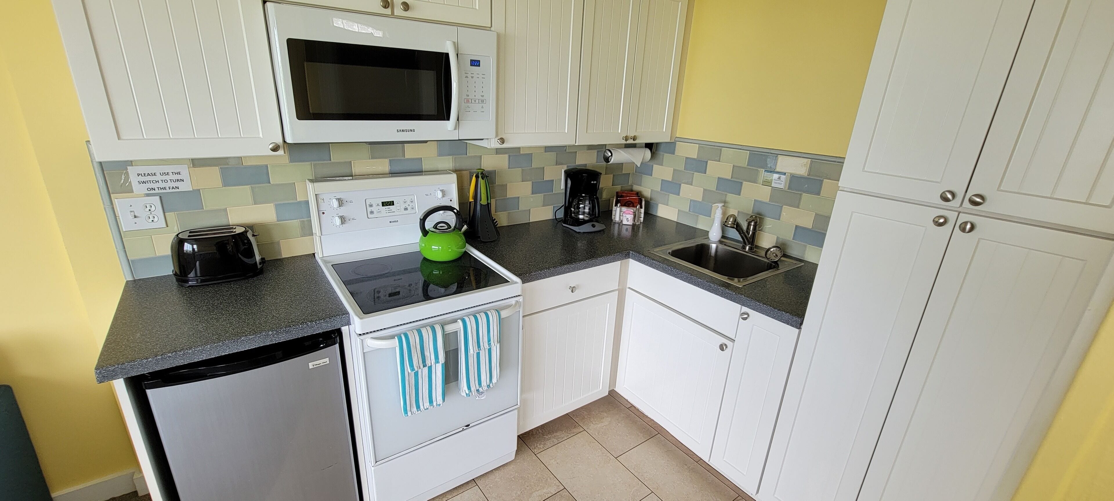 Una cocina compacta con microondas, tostadora, hervidor y fregadero.