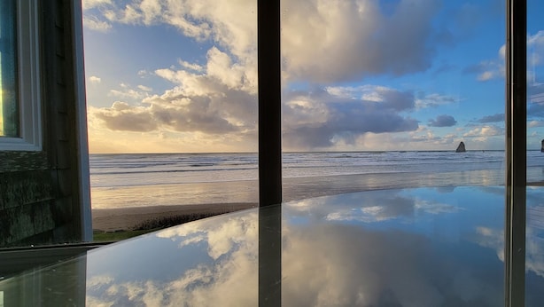 A beach view through a window with a clear sky and calm sea. - Sea Sprite at Haystack Rock (Cannon Beach)